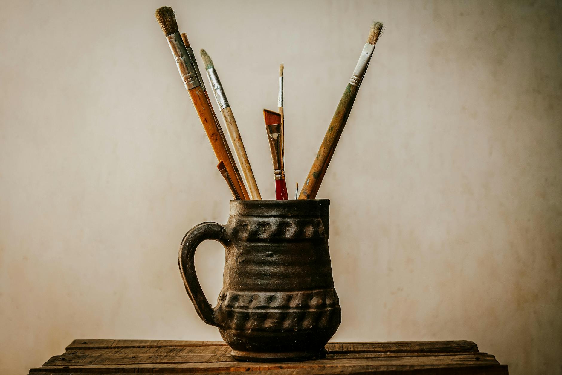 artistic paint brushes in ceramic jug on wooden table